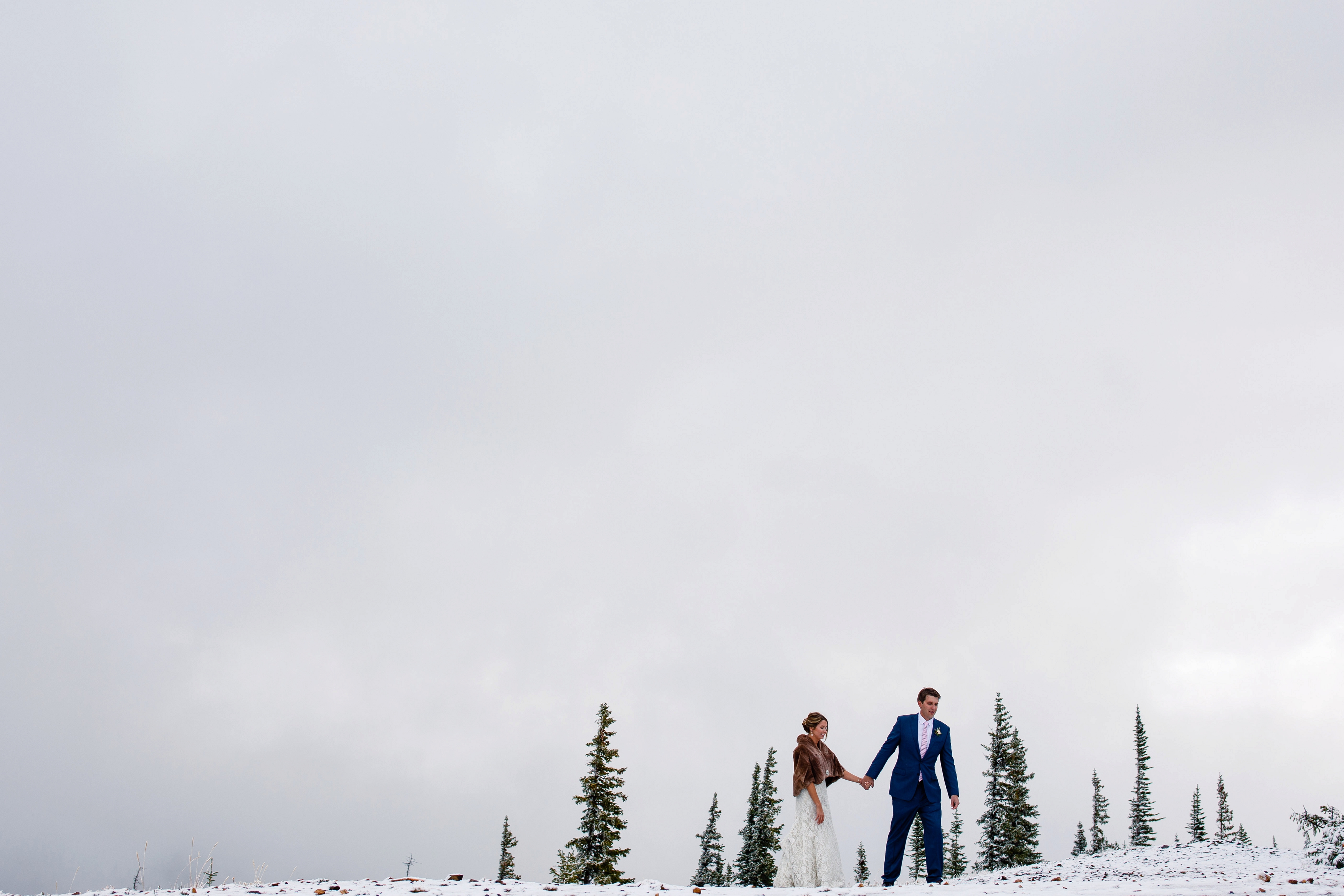 A bride & groom walk in the snow for their portraits during their Tenmile Station Fall Wedding. A bride & groom walk in the snow for their portraits during their Tenmile Station Fall Wedding.